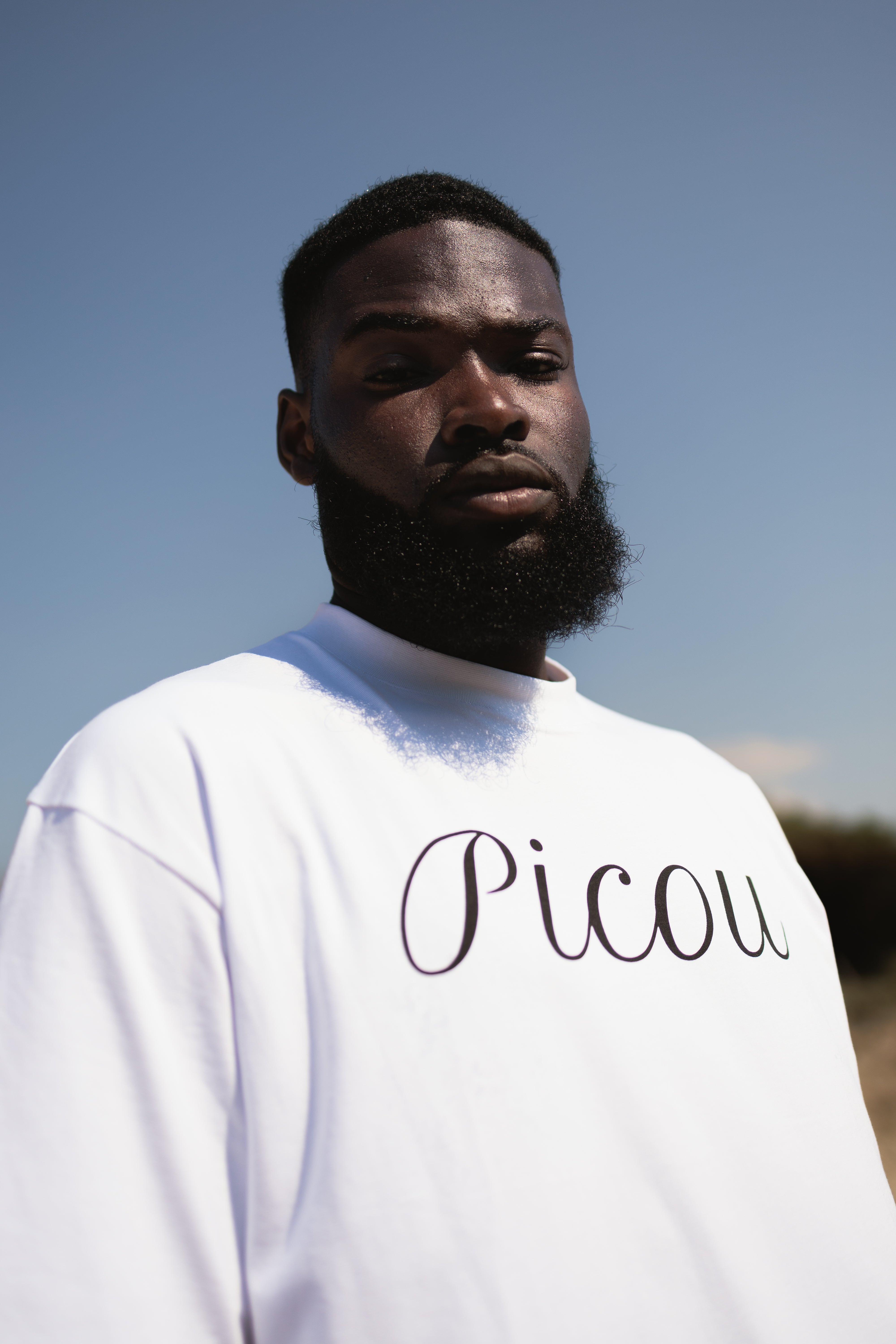 The Picou Cotton T-Shirt features the brand name elegantly written in cursive black letters across the front on a plain white background. A versatile and stylish addition to any fashion-forward wardrobe.