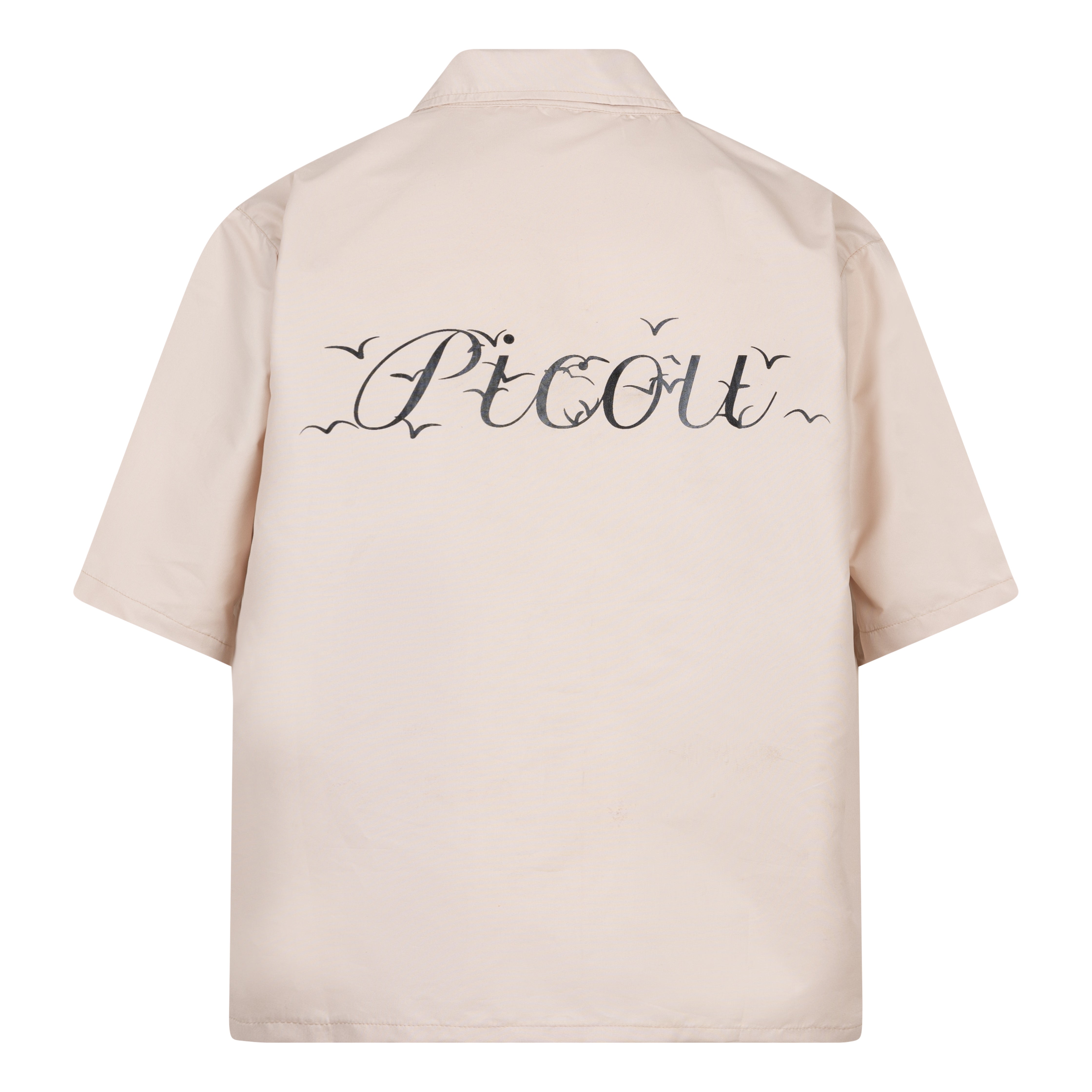 The Picou Nylon shirt in beige/cream is a short-sleeve button-up with a notched collar and a front pocket on the left chest. The pocket features a small metal tag design with intertwined letters in silver. This casual shirt offers a relaxed fit and is crafted from lightweight fabric, ideal for fashion-forward individuals seeking quality.